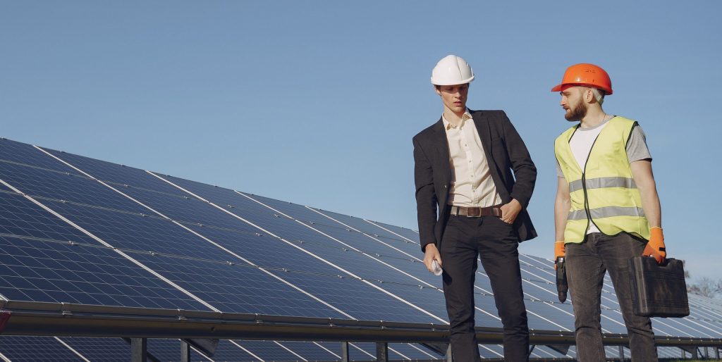 Dois homens conversando ao lado de painéis que produzem energia solar para a indústria.