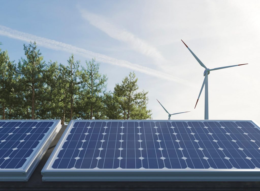 Painéis solares em um telhado, com turbinas eólicas e uma floresta ao fundo, sob um céu claro. A imagem destaca a integração de energia solar e eólica.