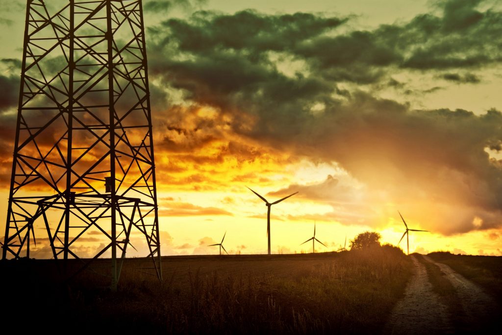 Uma paisagem rural ao entardecer com turbinas eólicas ao fundo, capturando a energia do vento.