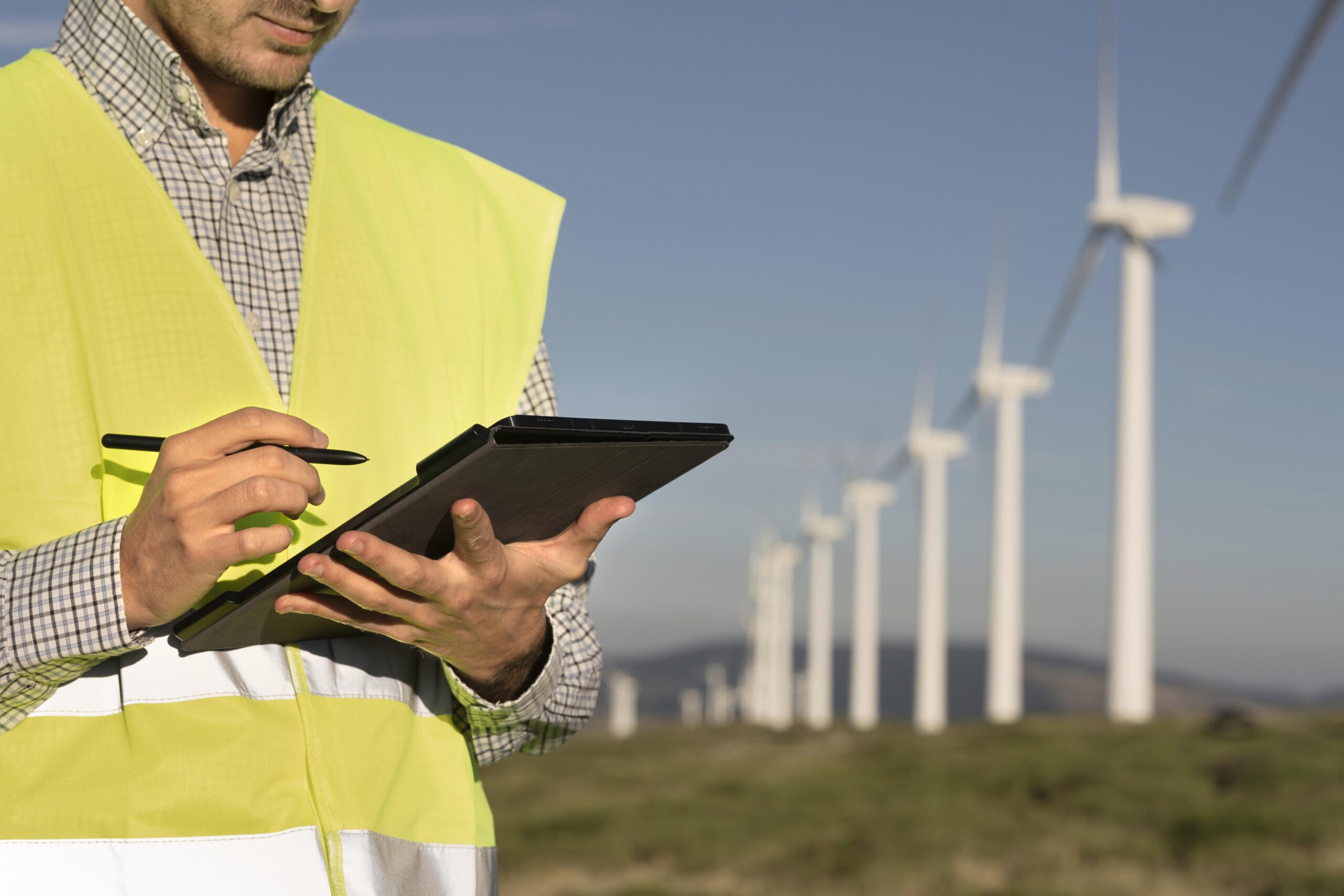 Homem mexendo em um tablet com caneta e um campo de energia eólica. Ilustrando o tema "Economia de Energia na Indústria".